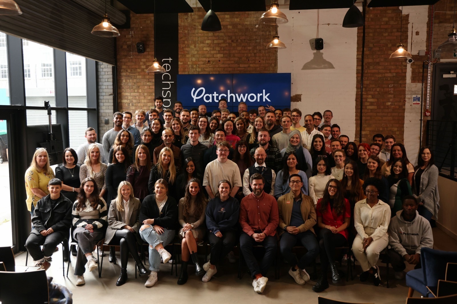 Patchwork colleagues gathered for a team photograph in a brick-walled event space
