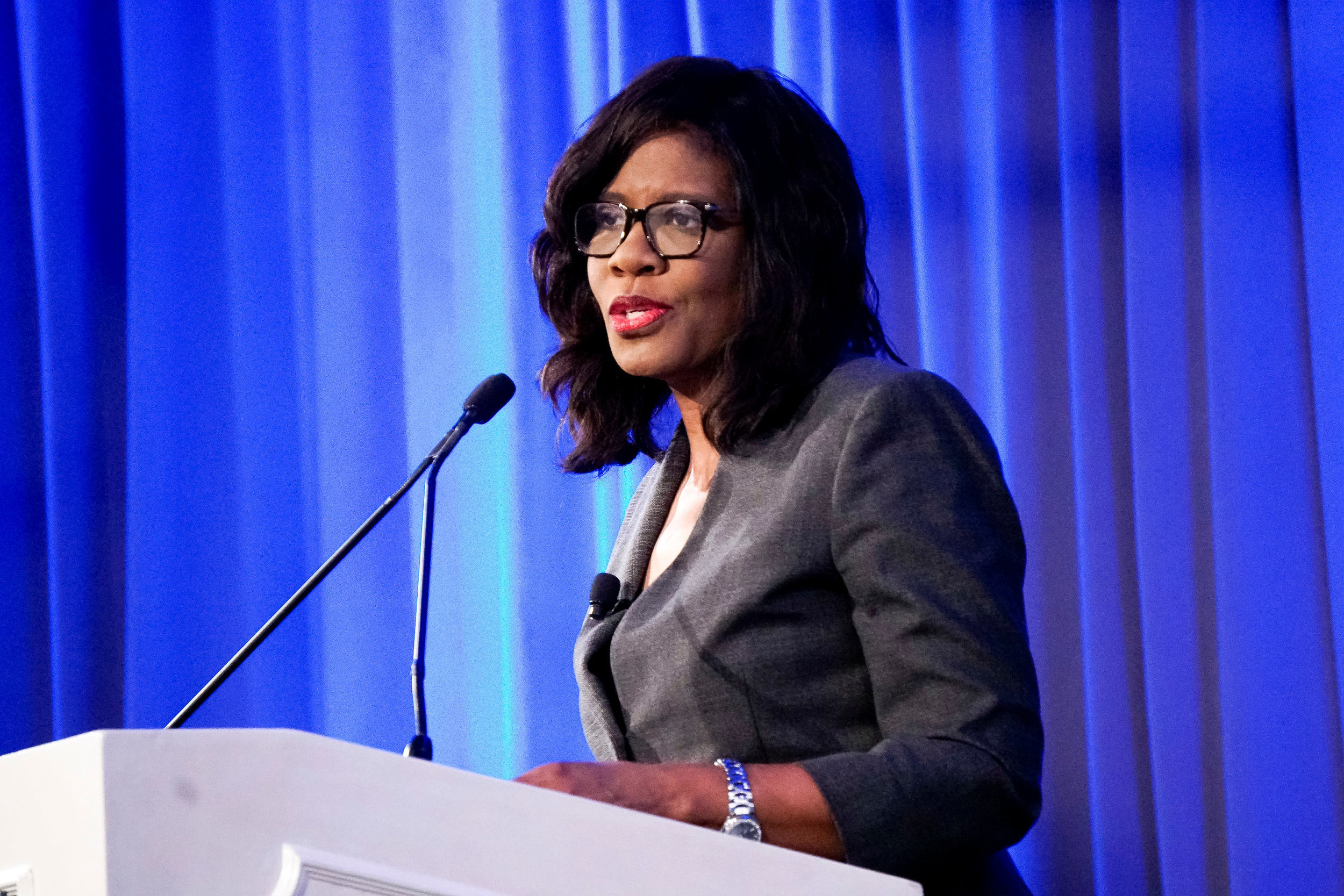Patrice Harris speaking at a lectern against a blue curtain