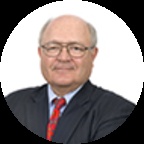 Patrick Caragata wearing glasses, a dark suit and a red patterned tie