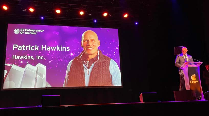 Patrick Hawkins at a lectern beside a screen displaying his name at the EY Entrepreneur Of The Year event