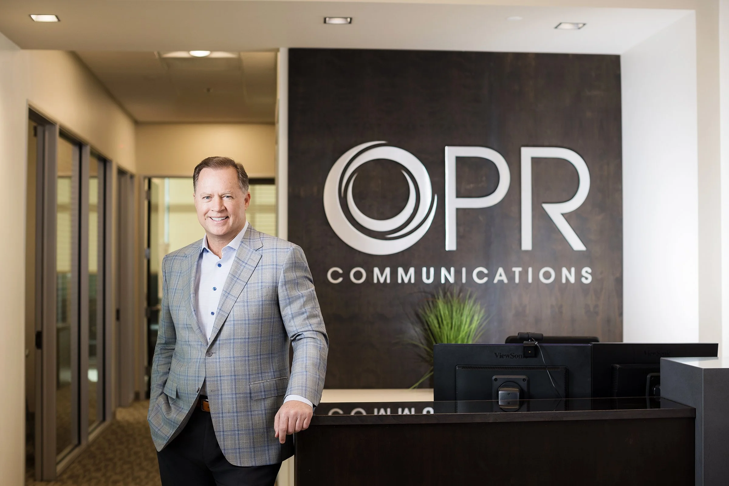 Patrick O’Reilly standing beside the reception desk beneath OPR Communications signage