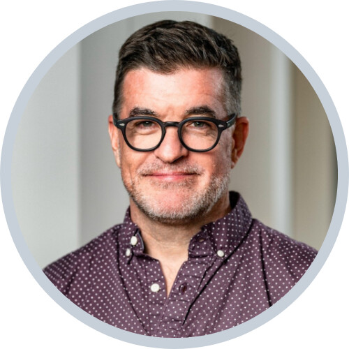 Patrick Reynolds smiling in glasses and a patterned shirt