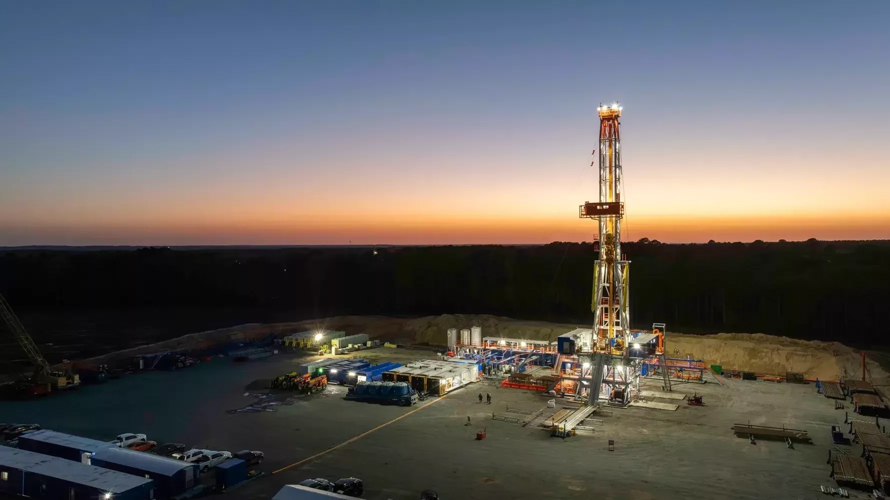 An illuminated Patterson-UTI drilling rig and its equipment spread across a wellsite at dusk