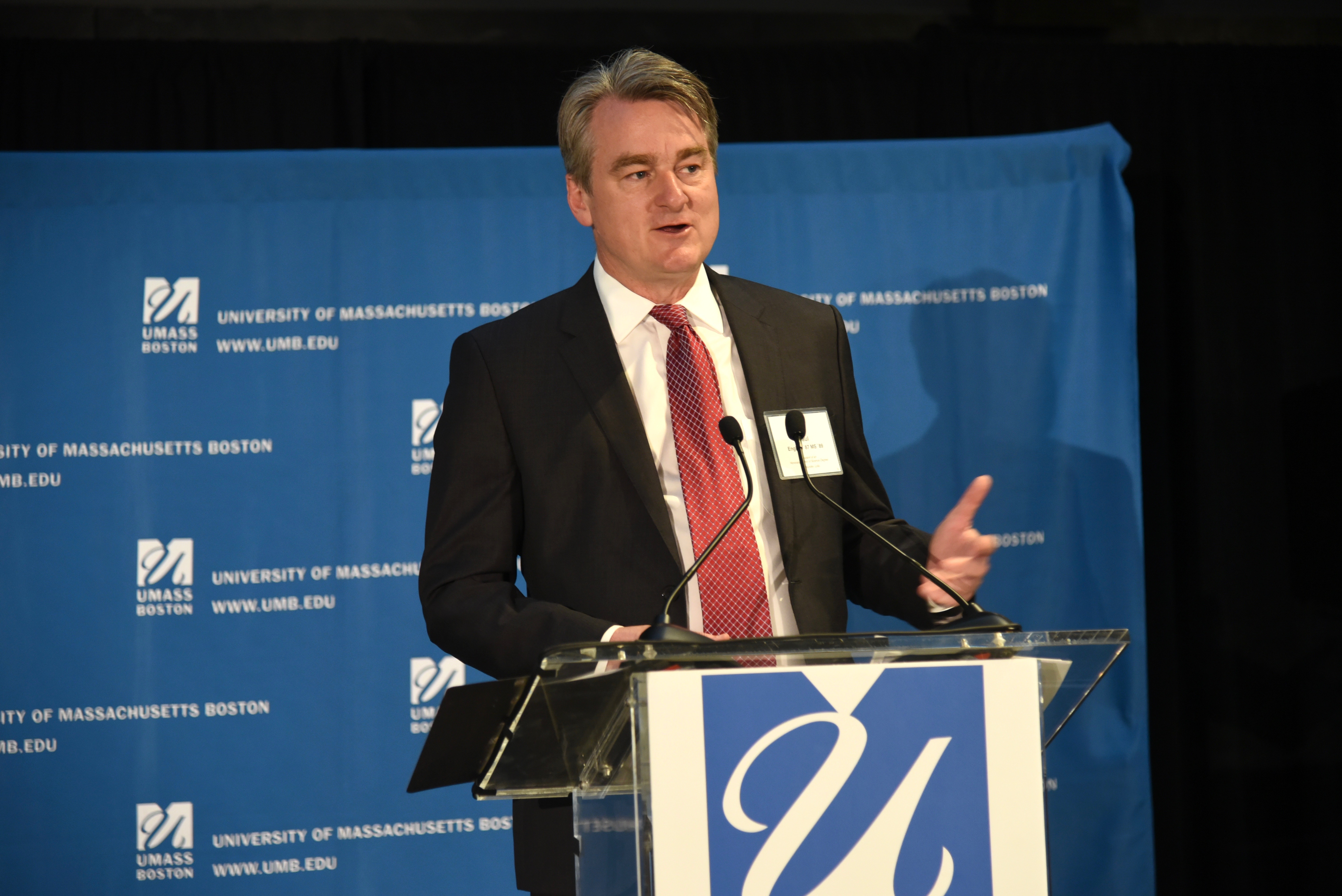 Paul English speaking at a lectern at the University of Massachusetts Boston
