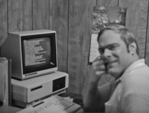 An archival photograph of Paul Hawkins beside a Tandy computer