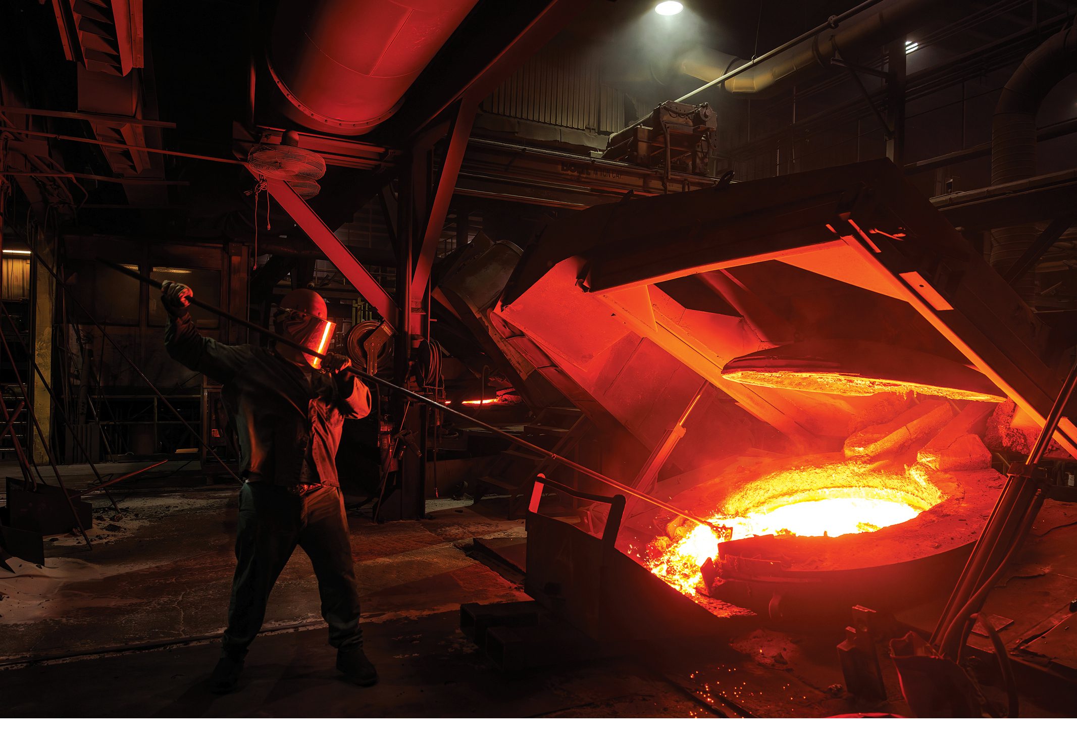 A worker beside a glowing ladle of molten metal inside a Mueller foundry