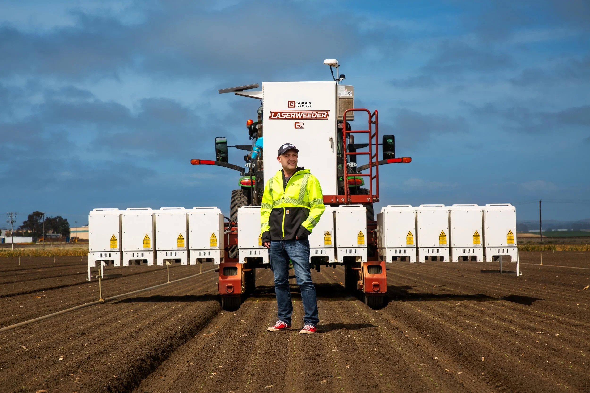 Paul Mikesell standing in a cultivated field in front of a Carbon Robotics LaserWeeder G2
