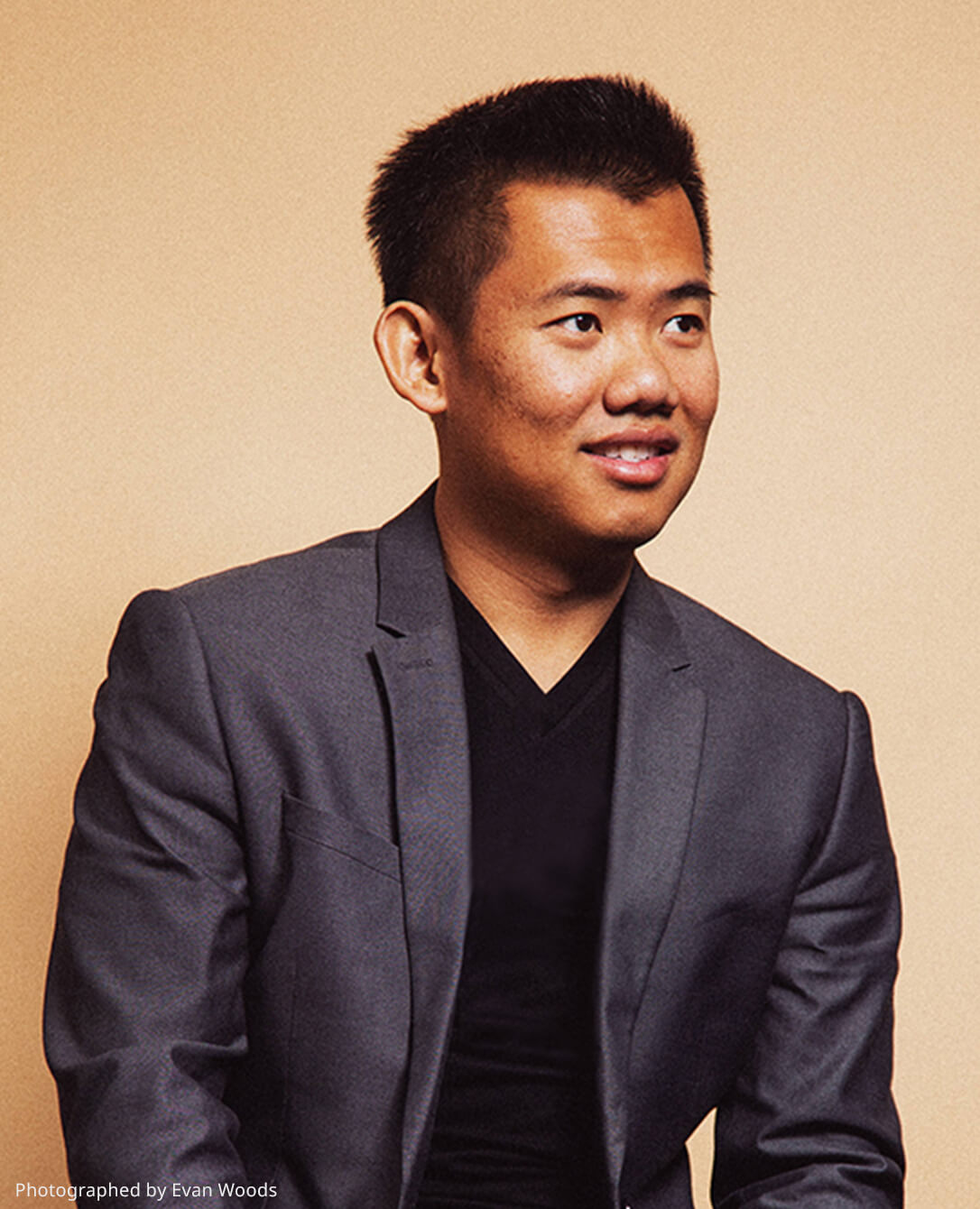 Paul Tran seated in a dark blazer against a warm neutral background
