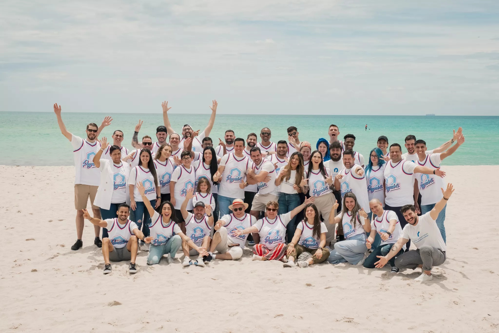 Payabli team members gathered on a beach wearing matching company jerseys