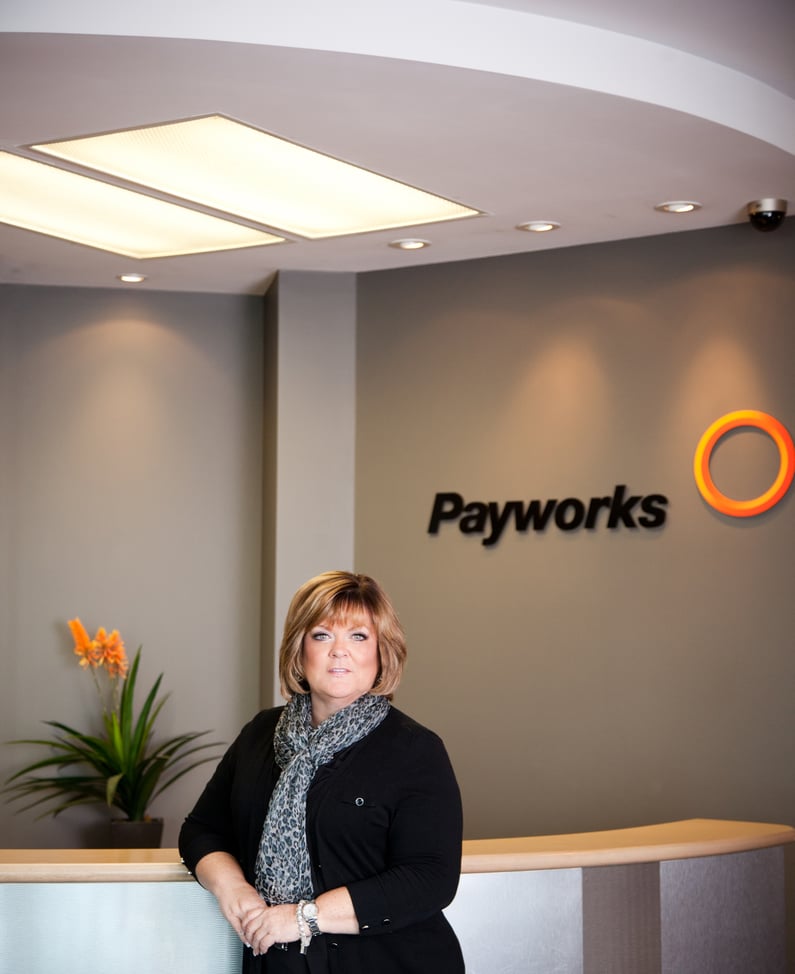 Payworks co-founder Barb Gamey stands in an early Payworks office beside a reception desk and company sign.
