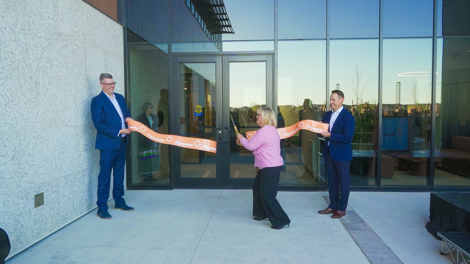 Barb Gamey cuts an orange ribbon outside Payworks' new Winnipeg headquarters as Michael Penman and JP Perron hold the ends.