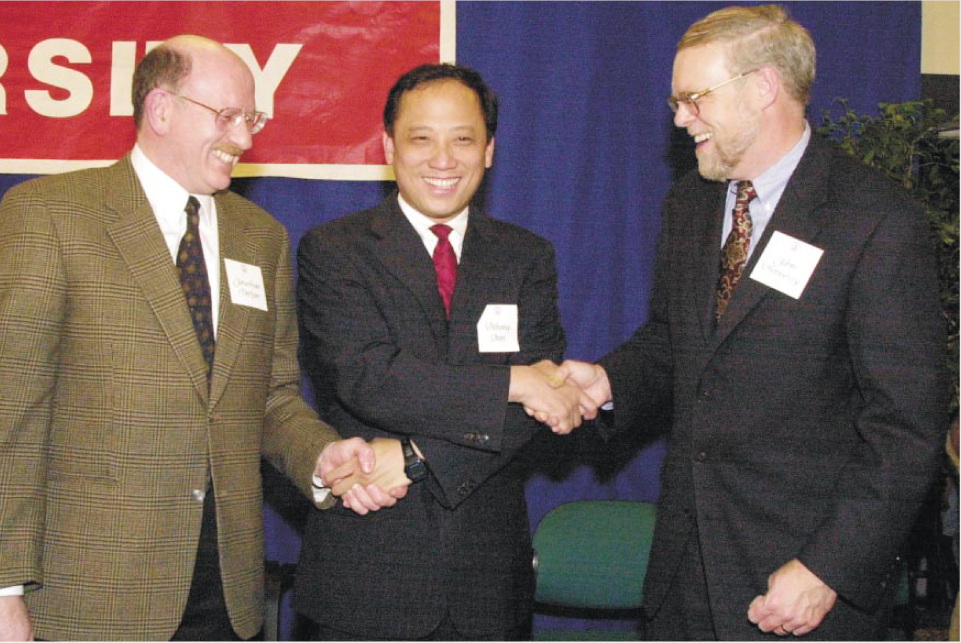 Pehong Chen smiles between Jonathan Dorfan and John Hennessy, shaking hands with both at the Stanford institute announcement.