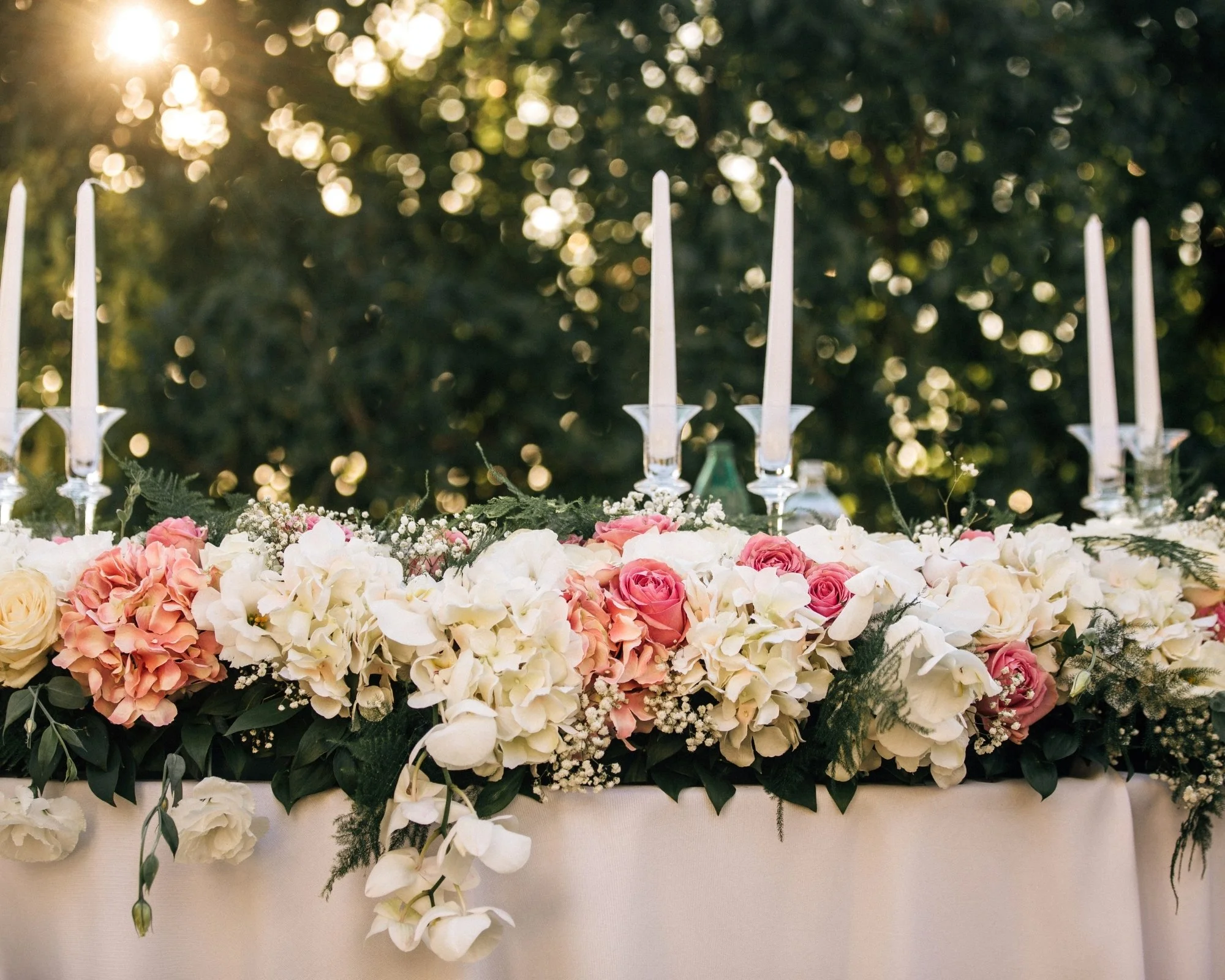 Pink and white flowers arranged beneath tall taper candles and hanging glass ornaments