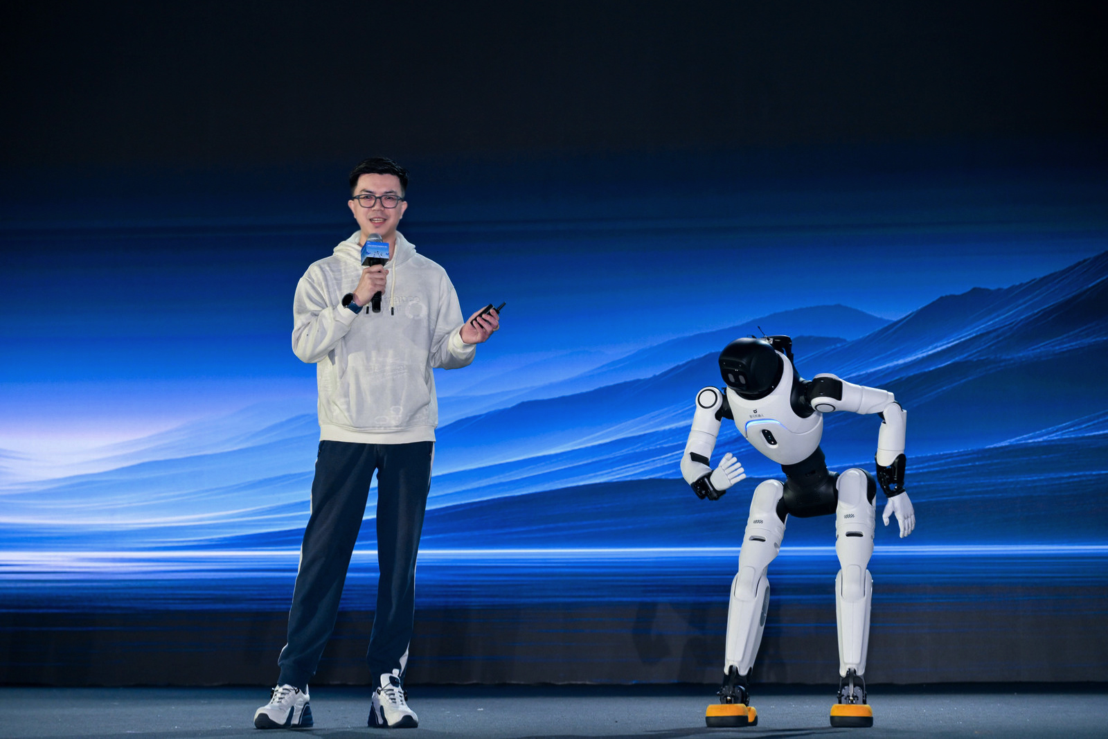 Peng Zhihui speaks on stage beside an AgiBot X2 humanoid robot at the company's 2026 partner conference