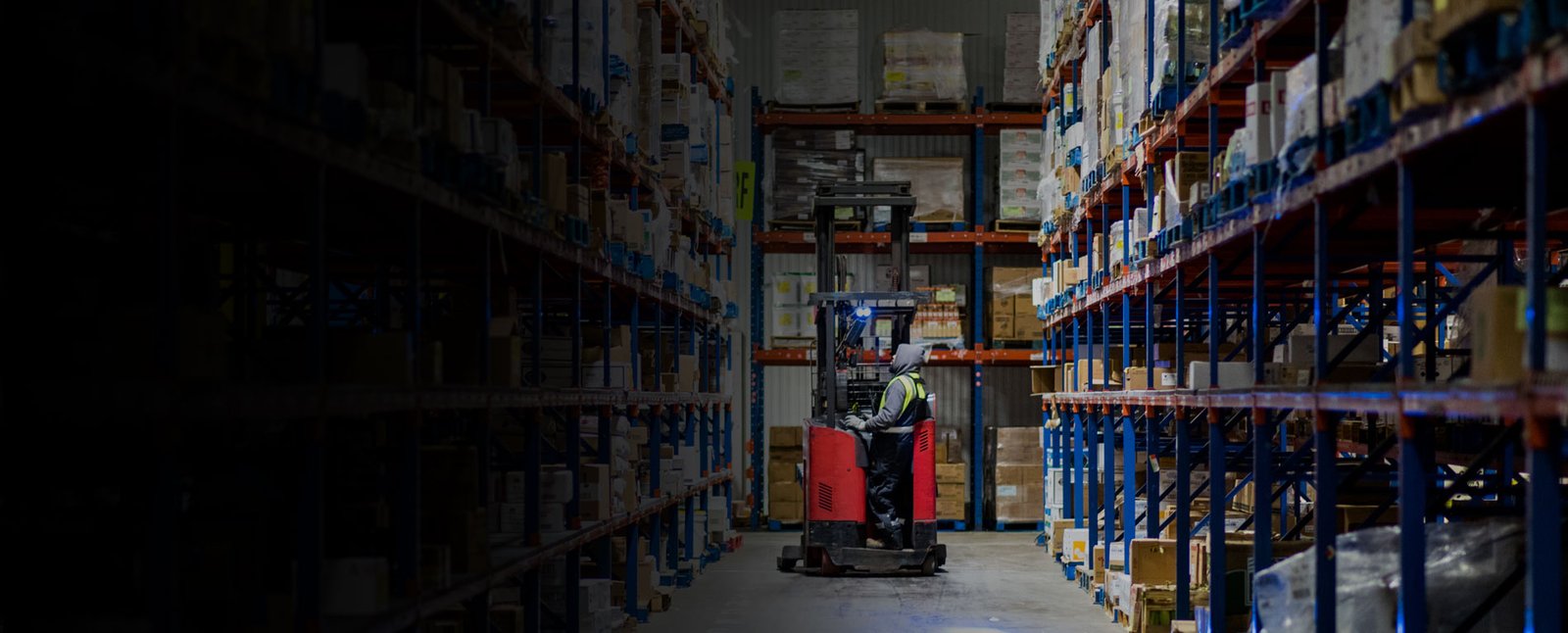 A warehouse associate operates material-handling equipment between tall shelves of inventory