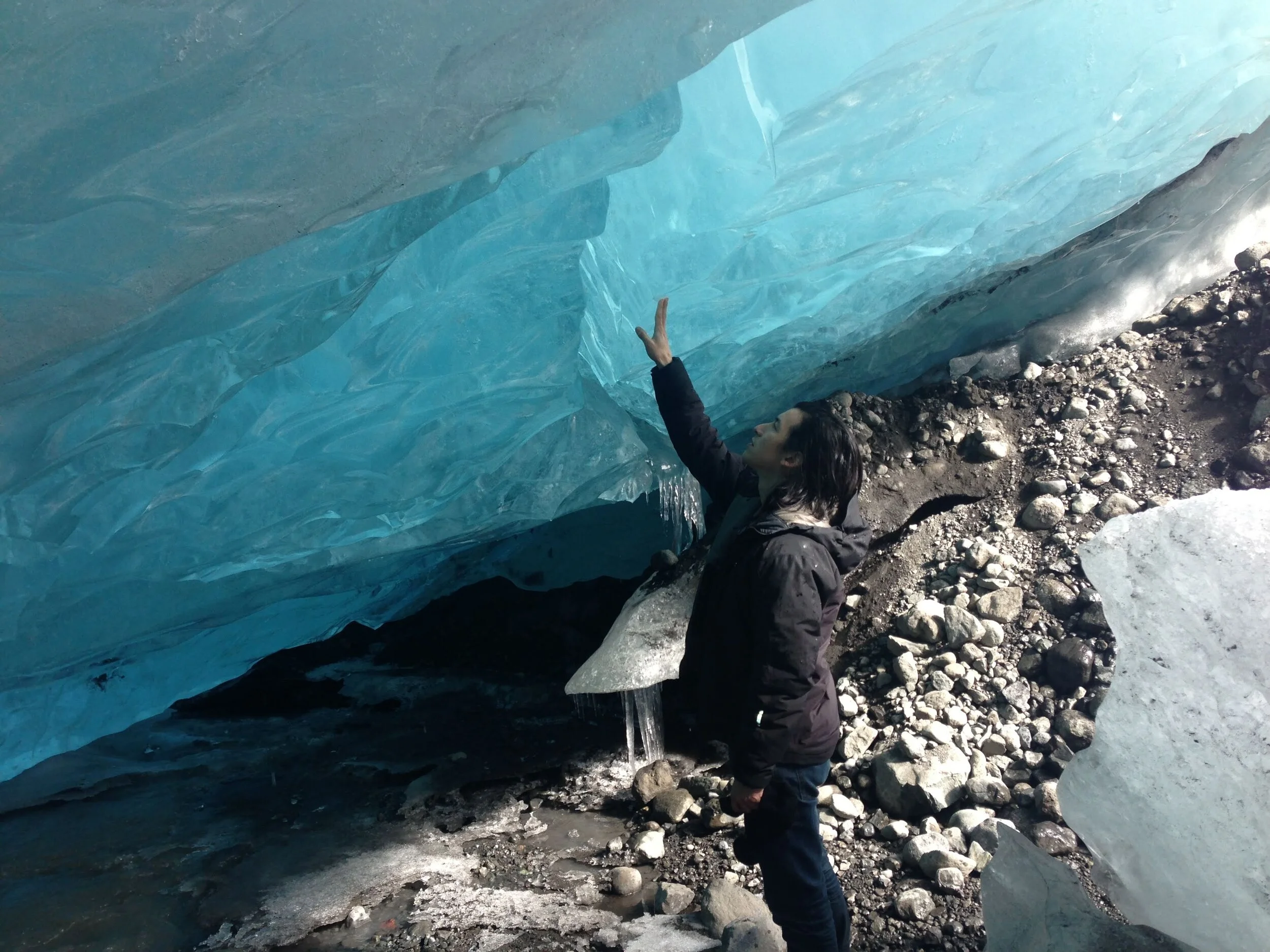Perry Chen standing beside a wall of blue ice in Iceland, reaching upward with one hand.