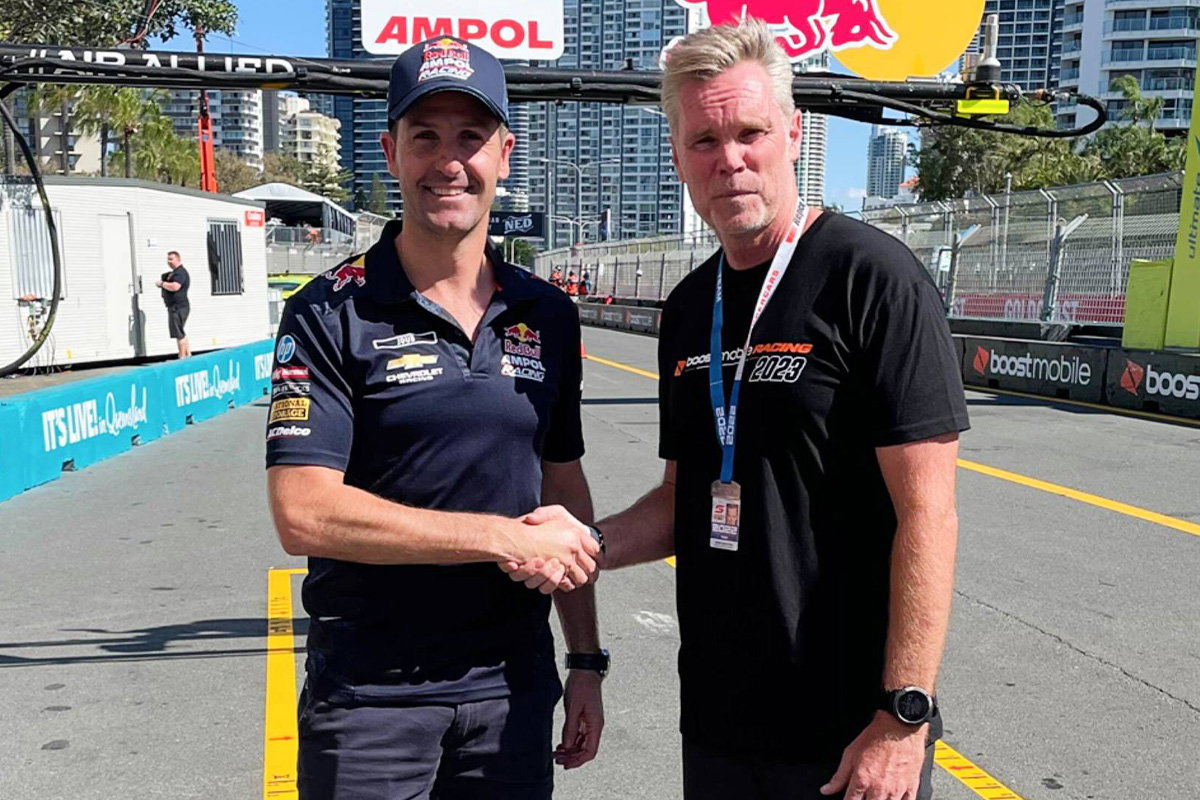 Jamie Whincup, left, shakes hands with Peter Adderton at a motor racing circuit.