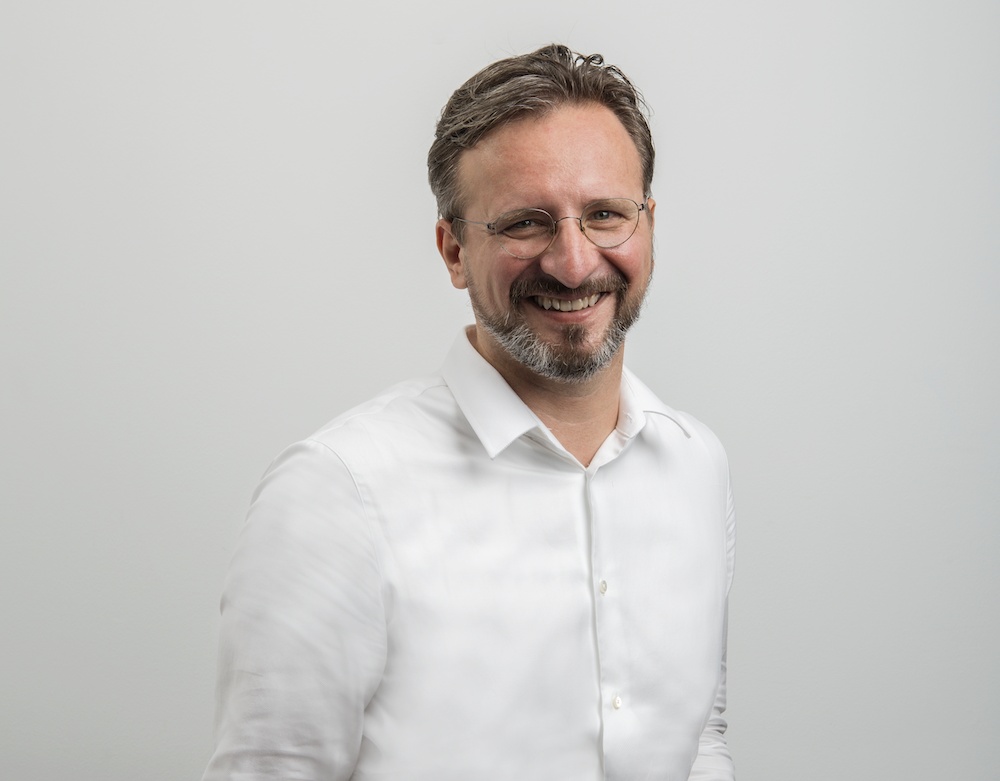 Peter Barcak wearing glasses and a white shirt, smiling in a press photograph