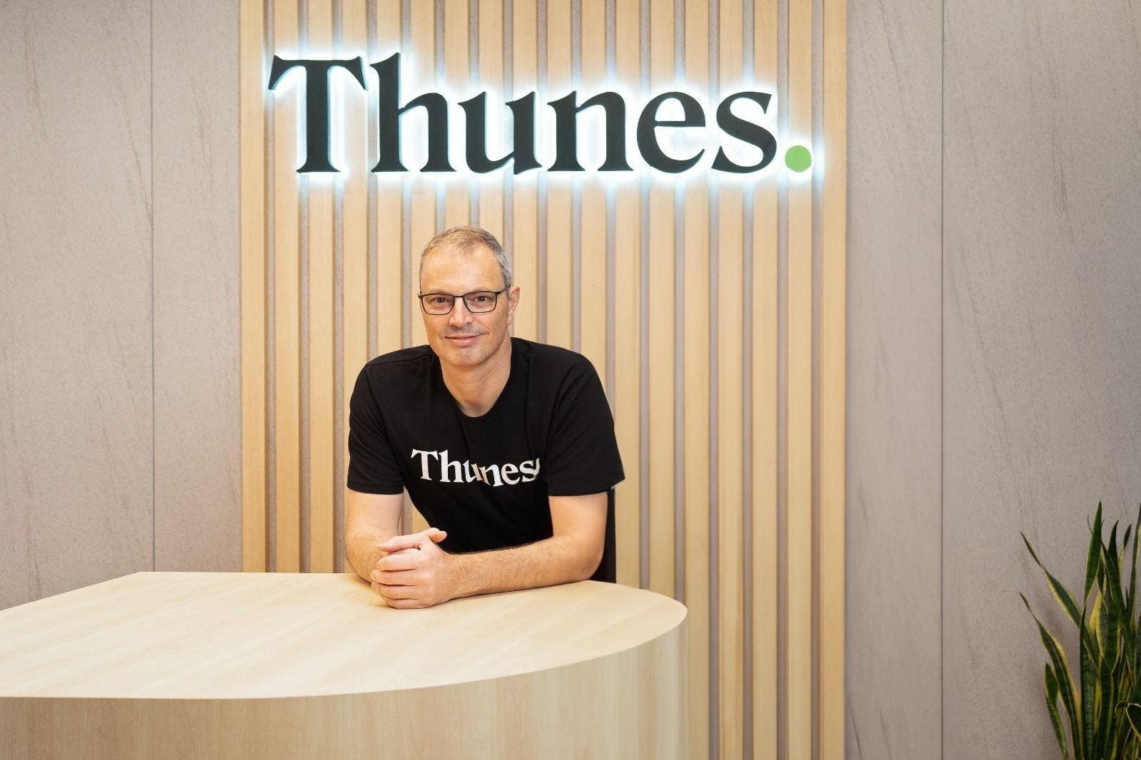Peter De Caluwe seated at a table in a Thunes office, wearing a black Thunes T-shirt