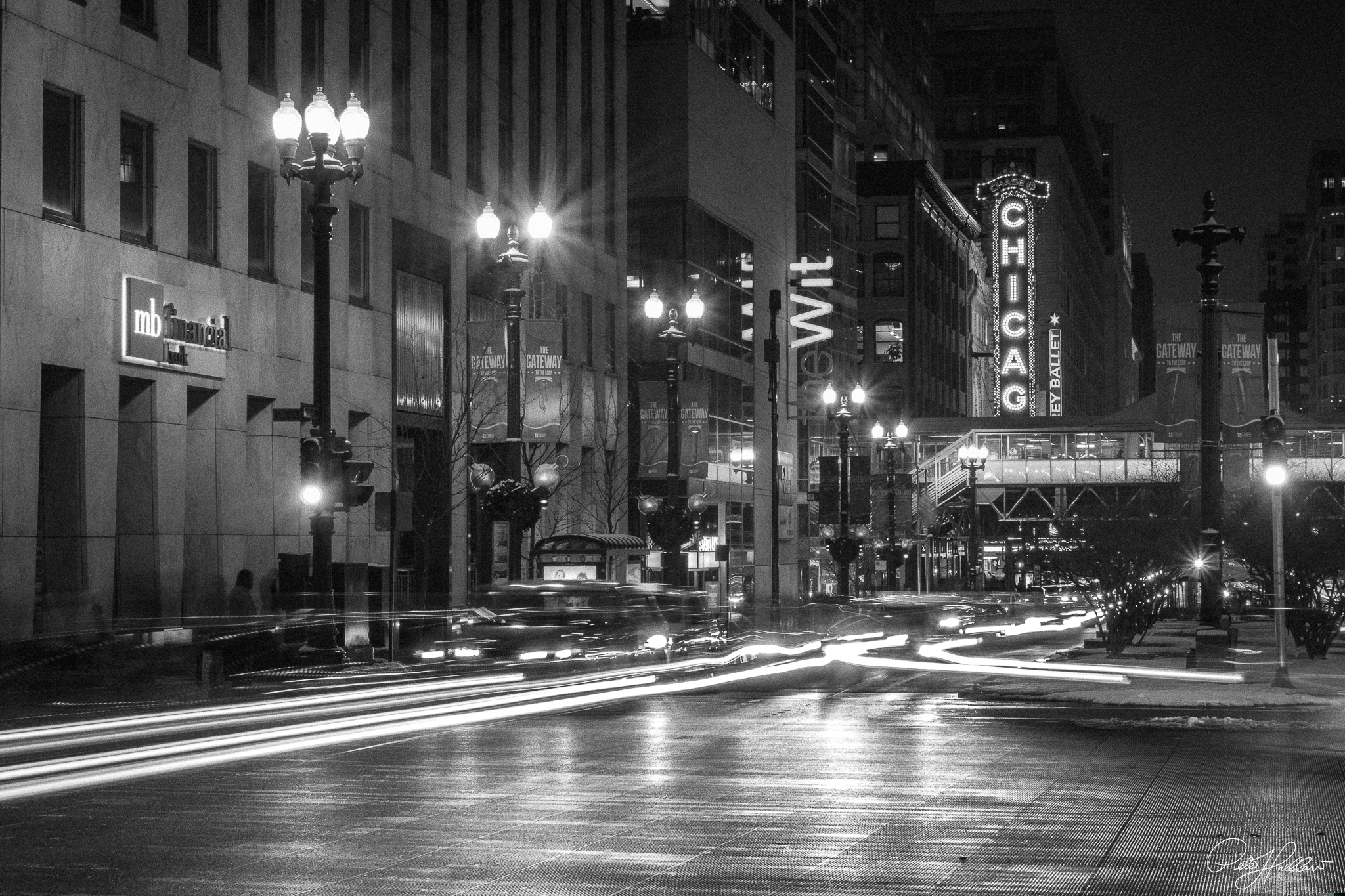 Black-and-white long exposure of downtown Chicago at night, with traffic trails leading toward the Chicago Theatre sign