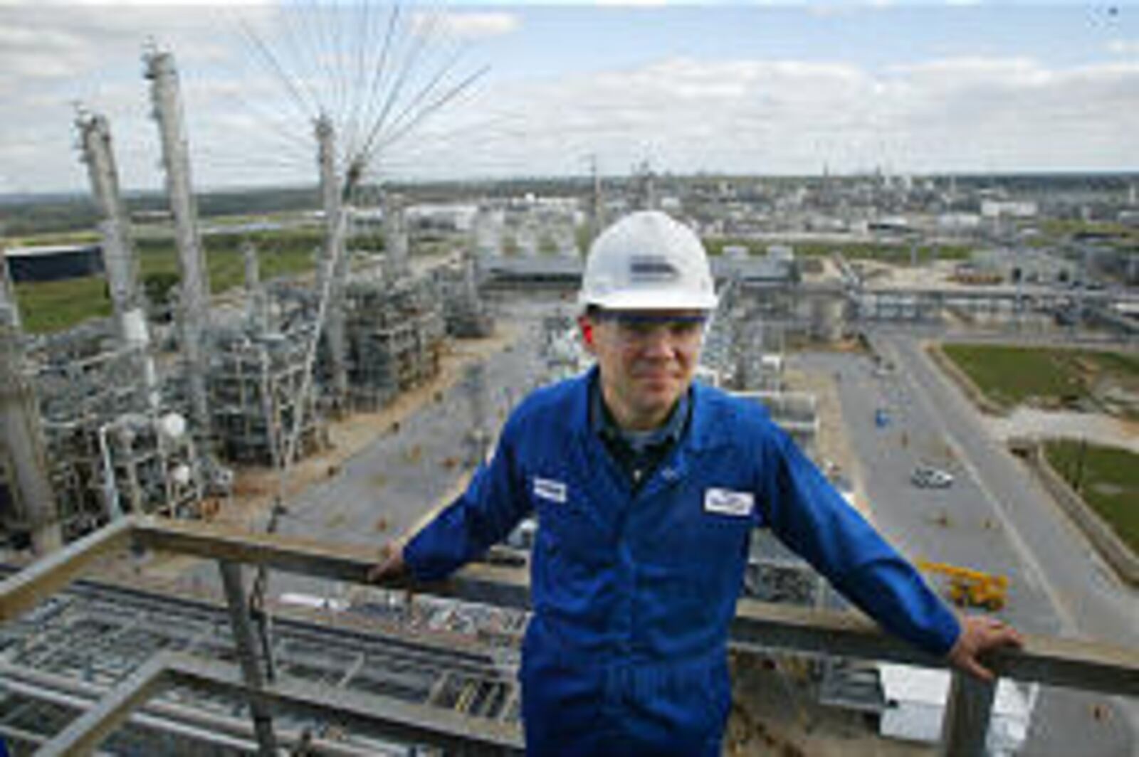 Peter Huntsman in blue workwear and a white hard hat overlooking a Texas petrochemical facility