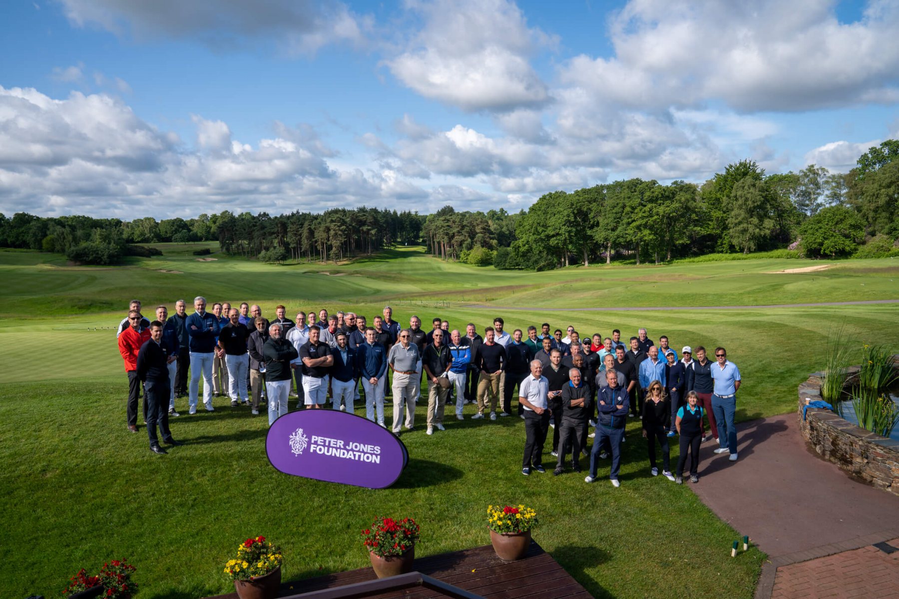 A group of participants gathered on a golf course behind a Peter Jones Foundation sign