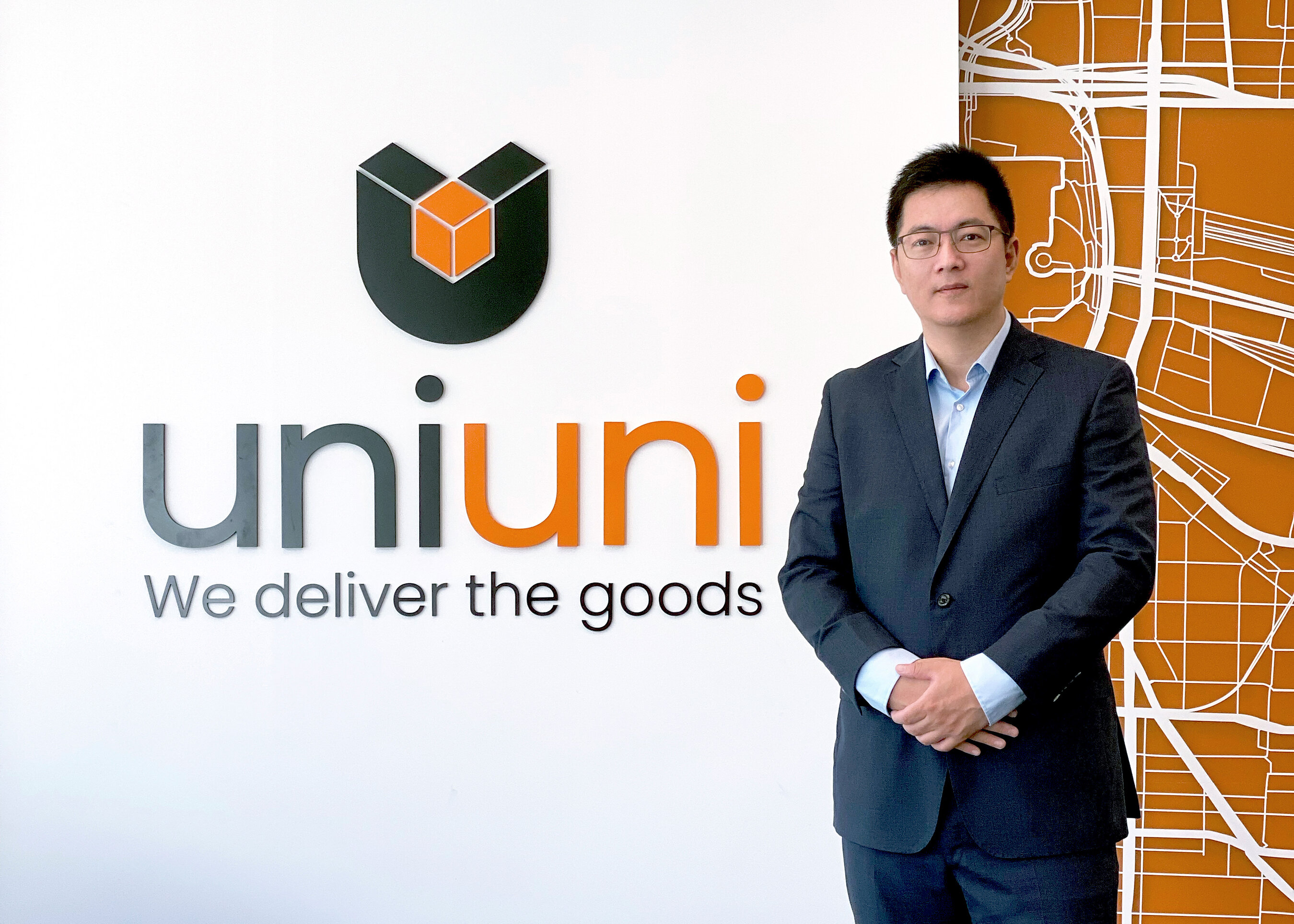 Peter Lu standing beside UniUni’s wall signage and an orange street-map graphic