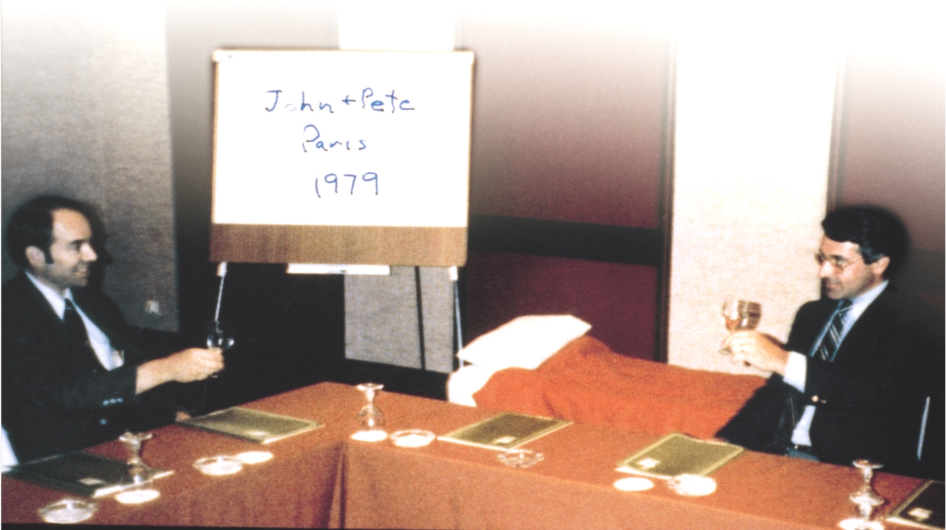 John Abele and Peter Nicholas seated at a table in Paris in 1979