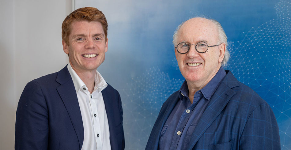 James Magill and Peter O'Connell stand together in front of a blue backdrop.