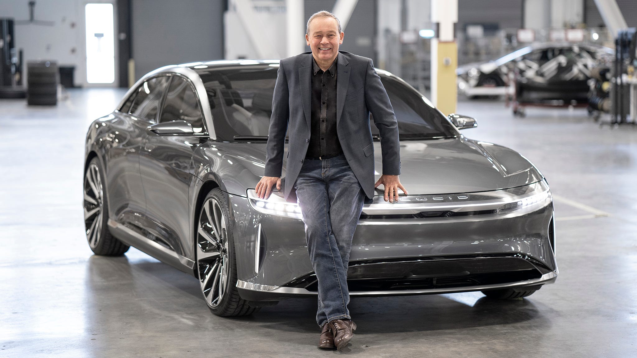 Peter Rawlinson smiling beside a silver Lucid Air in an automotive workshop
