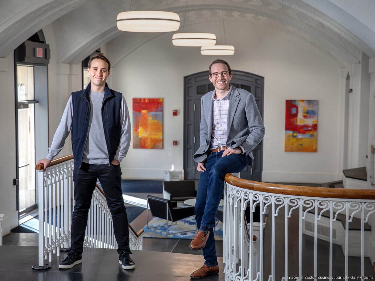 Peter Ross, left, and Nick Riotto at 829 Studios, standing and sitting beside an office railing.