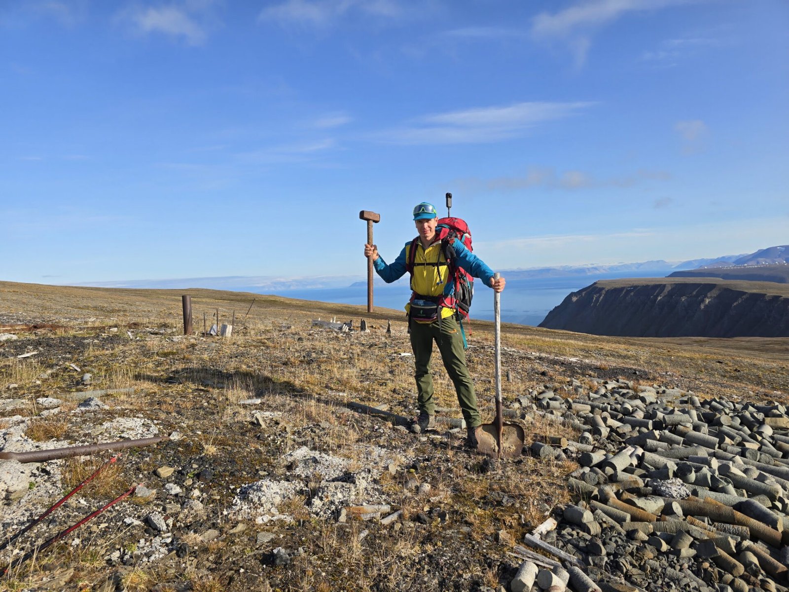 Peter Zaitsev with a backpack, holding old tools beside abandoned equipment in Svalbard