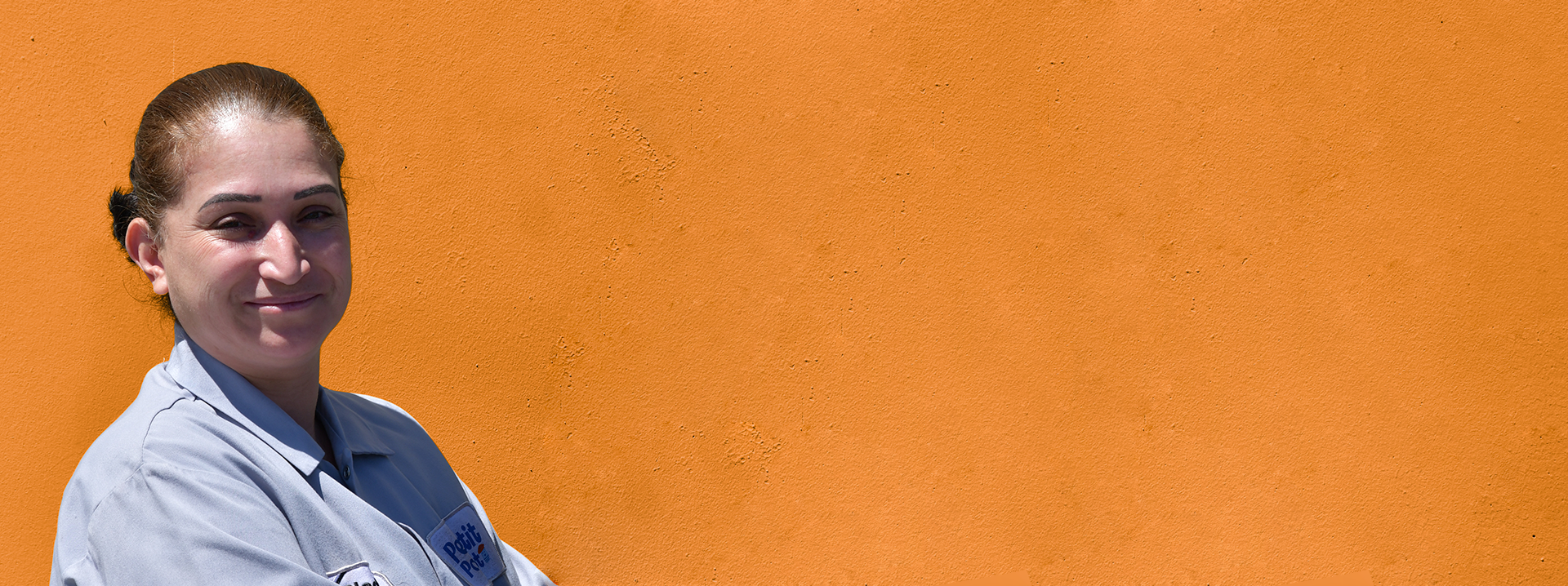 A member of Petit Pot’s production team wearing a work coat beside an orange wall