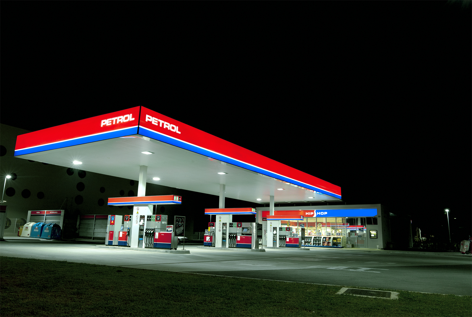 Illuminated Petrol fuel pumps and Hip Shop beneath a red and blue canopy at night