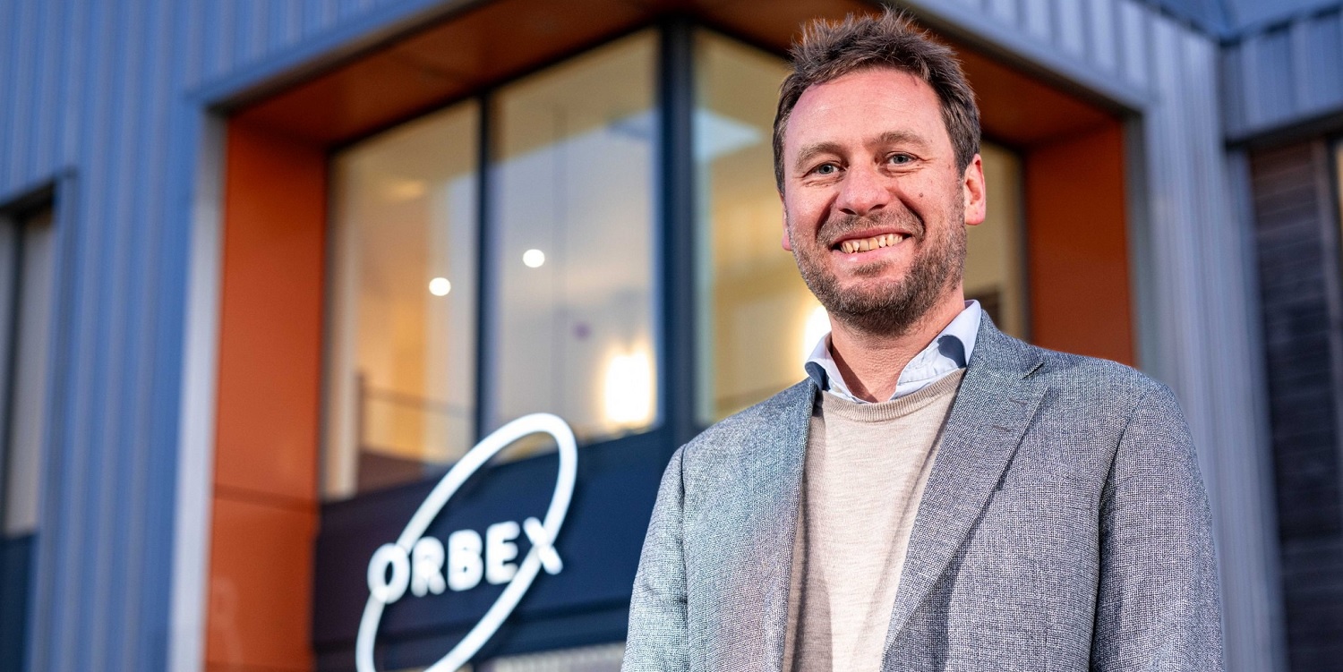 Phil Chambers outside an Orbex building, with the company’s orbital logo behind him