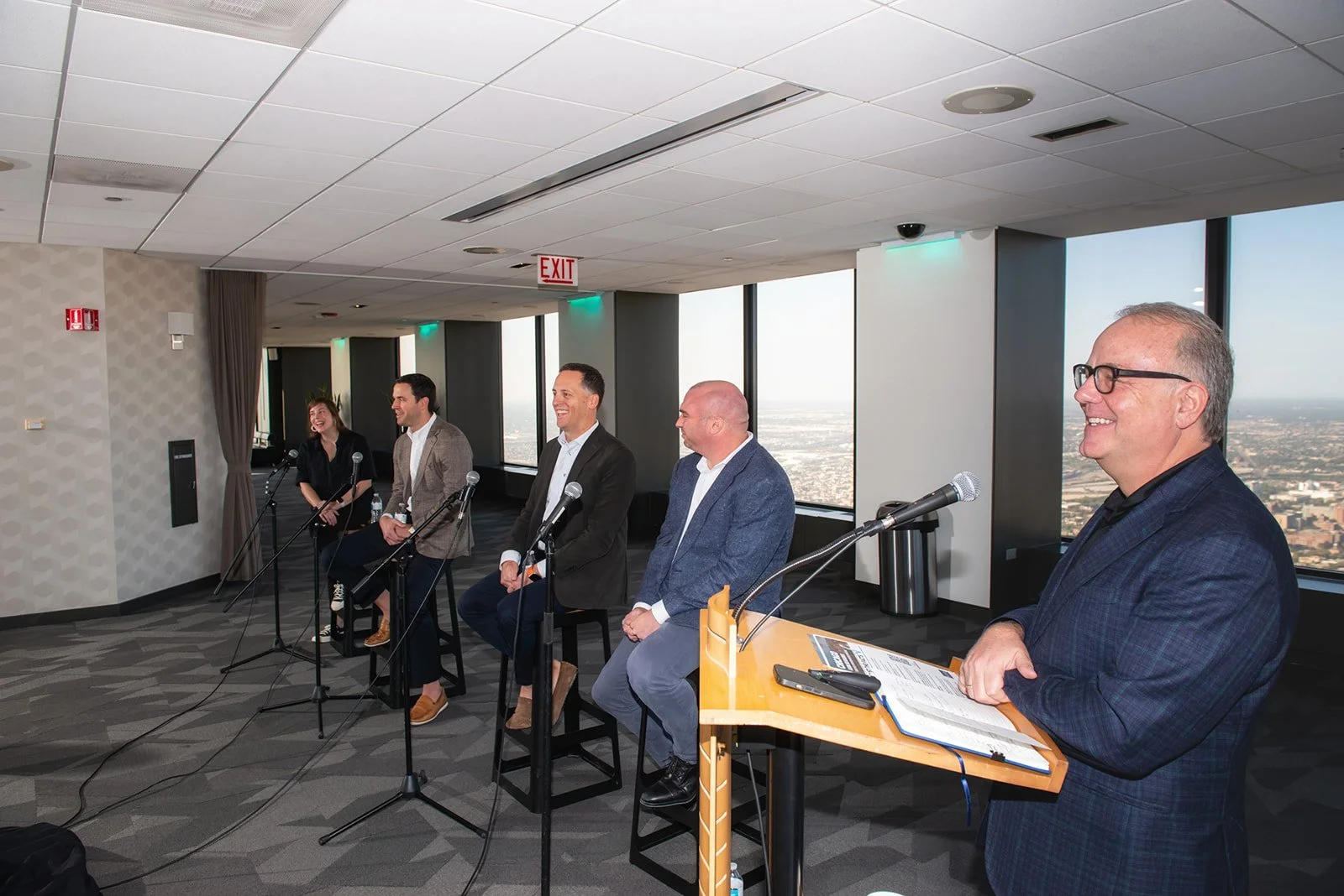 Phil Clement at a lectern on the right, moderating a panel beside windows overlooking Chicago