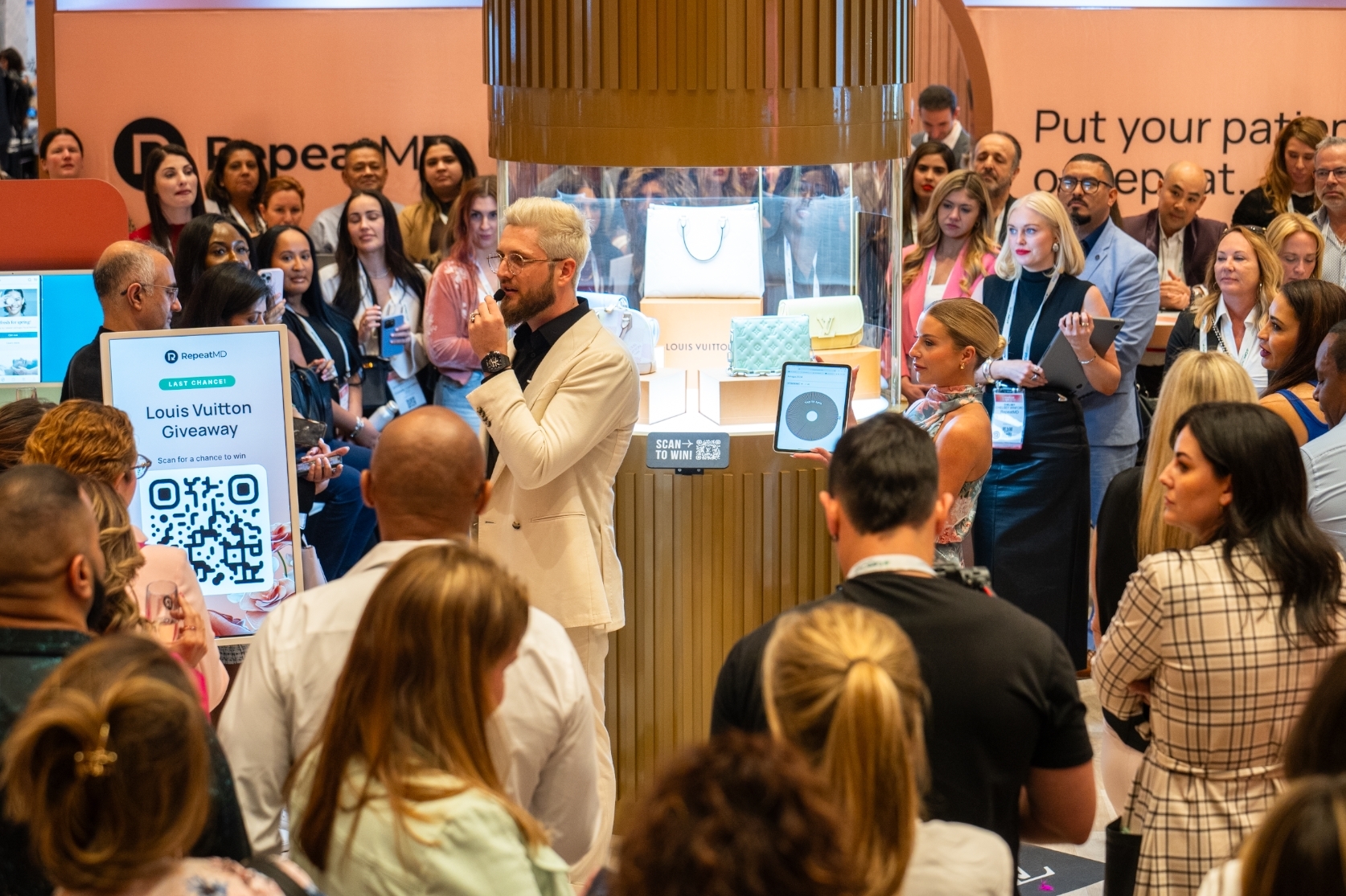 Phil Sitter speaking into a microphone to a crowd at a RepeatMD exhibition stand