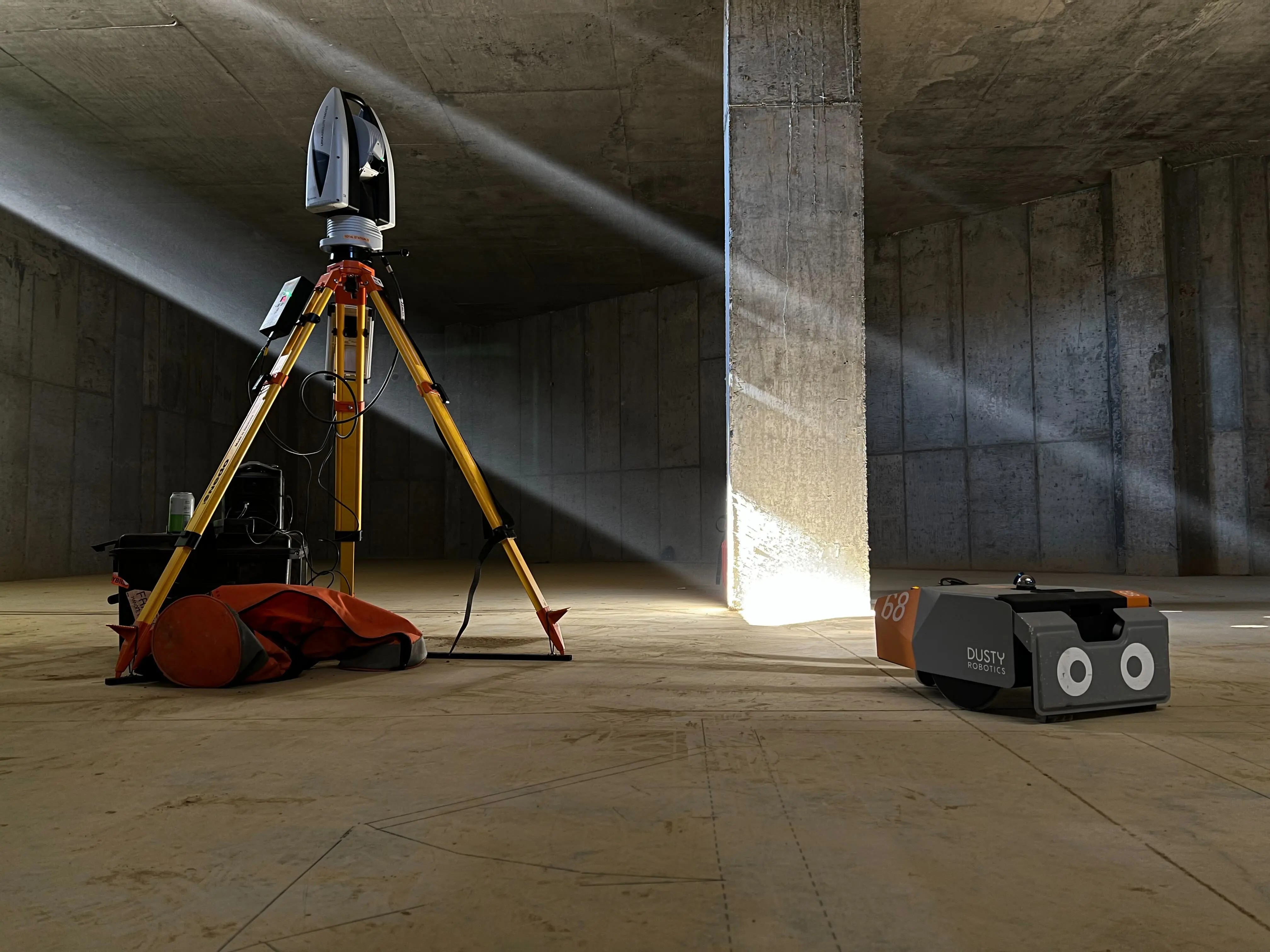 A Dusty Robotics FieldPrinter beside a surveying instrument on a concrete jobsite