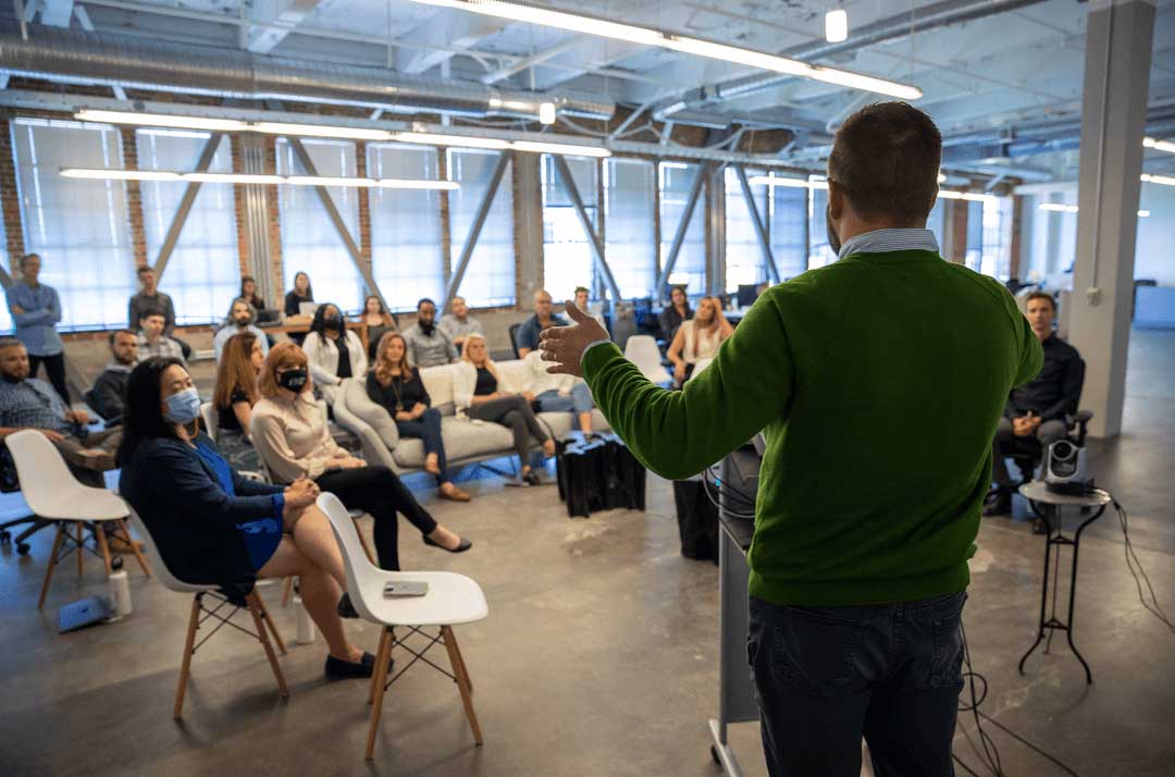 A pMD team gathered in an office, listening to a speaker