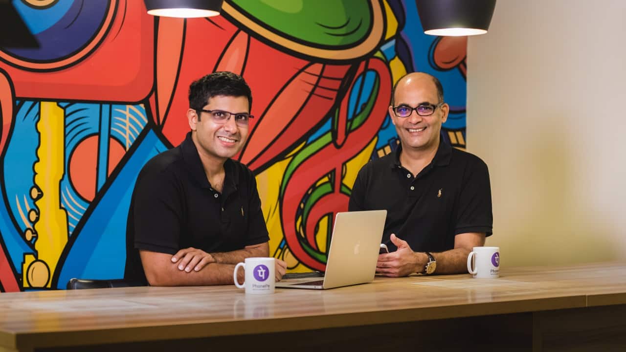 PhonePe co-founders Sameer Nigam and Rahul Chari seated at a table in front of a colorful office mural