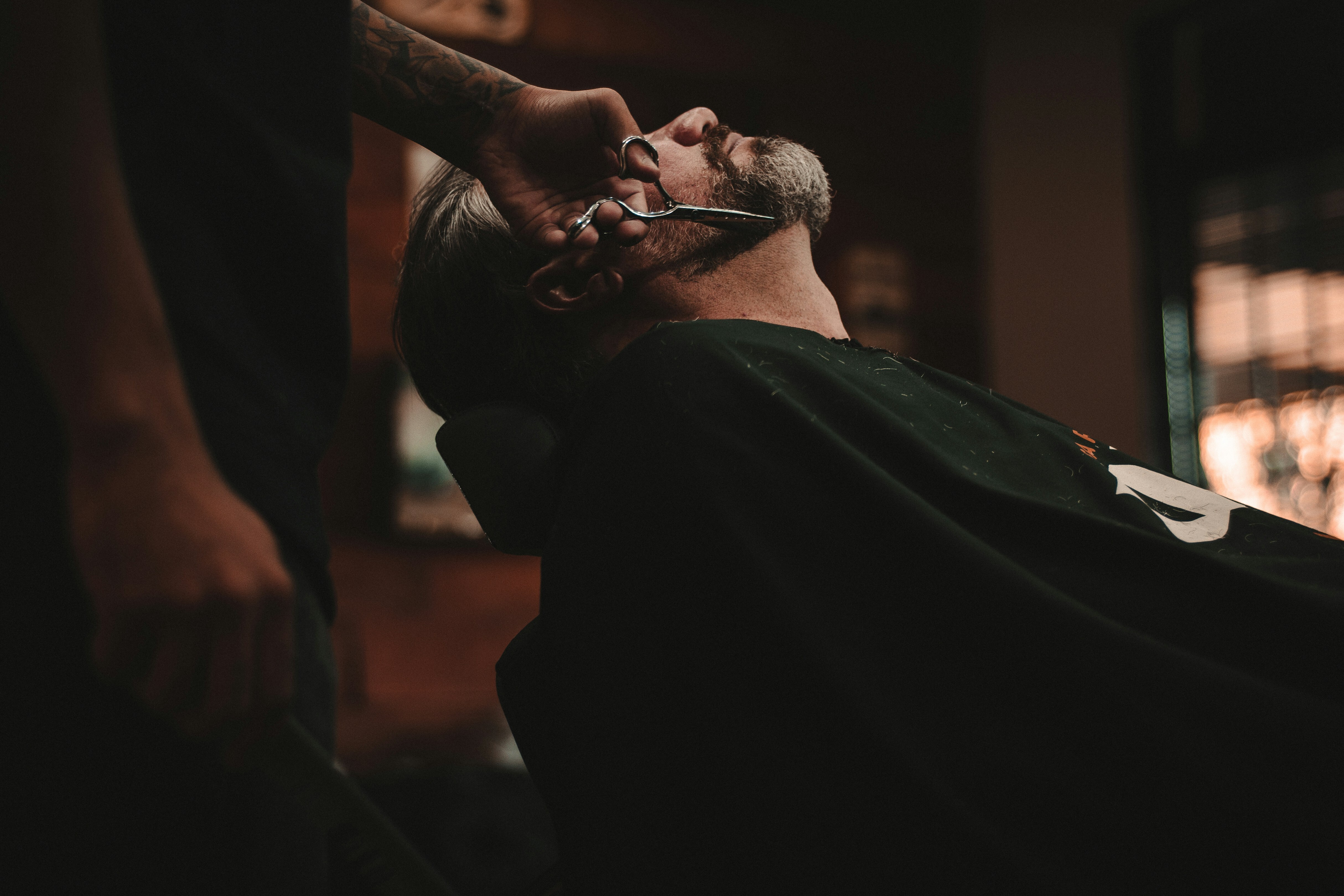A barber carefully trims a customer's beard