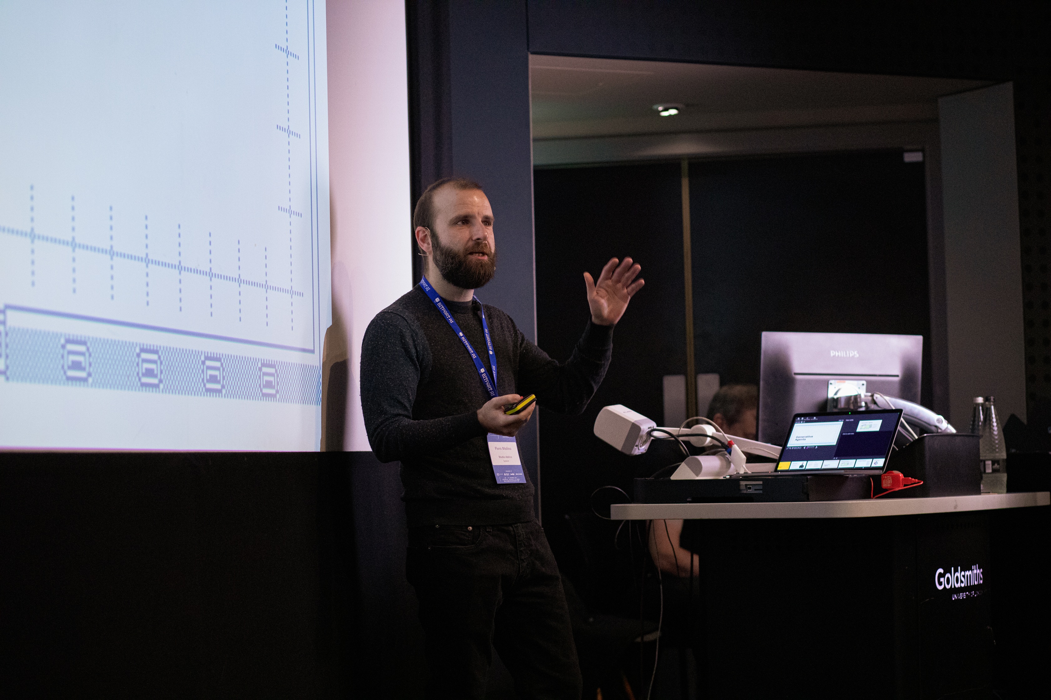 Piero Molino presenting beside a projected slide at the AI and Games Conference