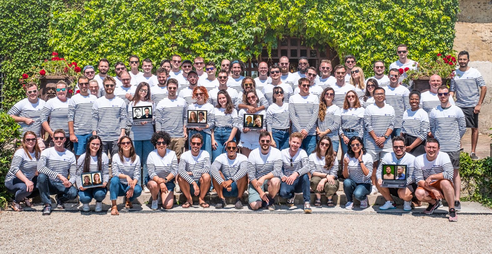Strapi colleagues gathered outdoors in matching striped shirts, holding laptops showing remote teammates