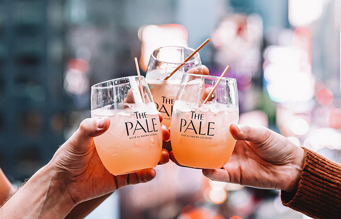 Three hands raising branded glasses of The Pale rosé spritz