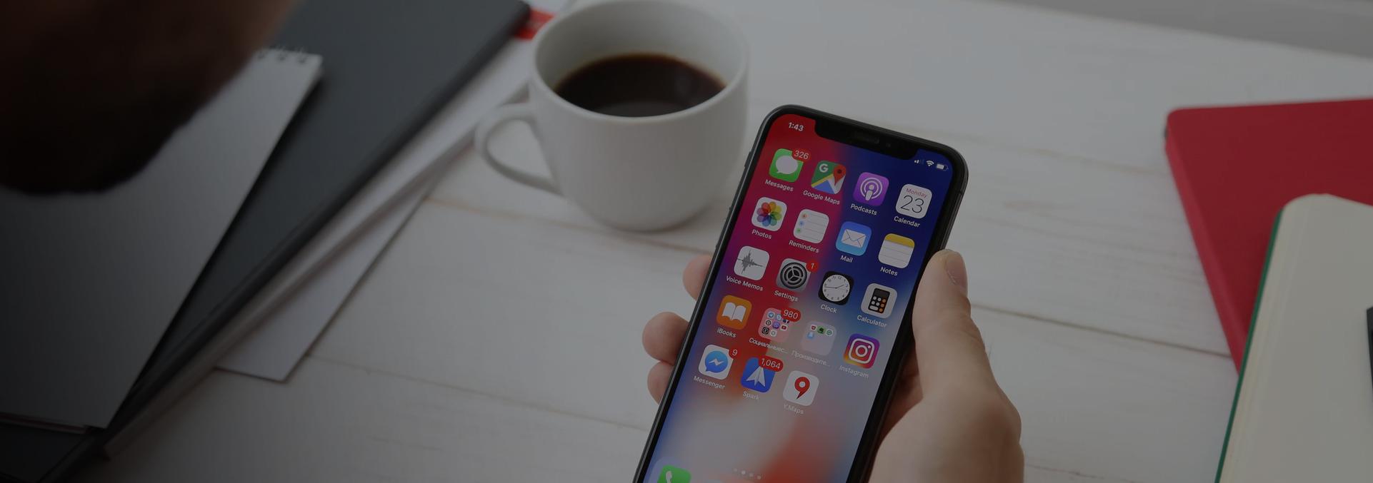 A smartphone beside a coffee cup and notebooks, from Pioneer’s mobile application services page