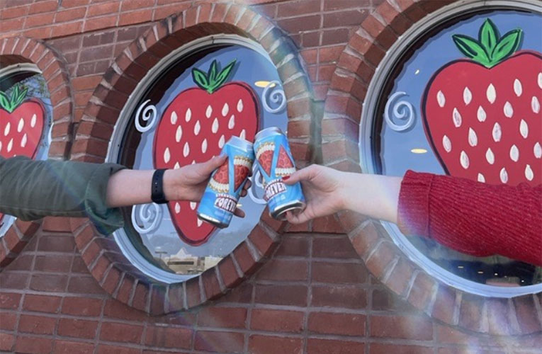 Two people toast cans of Strawberry Pie Forever beer outside Grist House