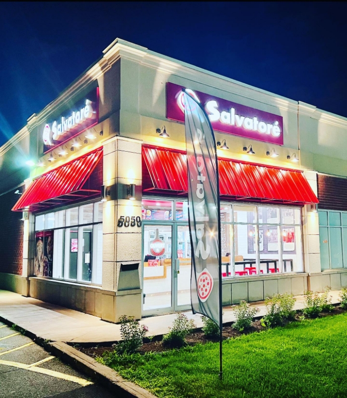 A brightly lit Pizza Salvatoré delivery and carryout storefront at night