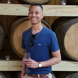 PJ Brown smiling in a casual blue shirt beside wooden barrels