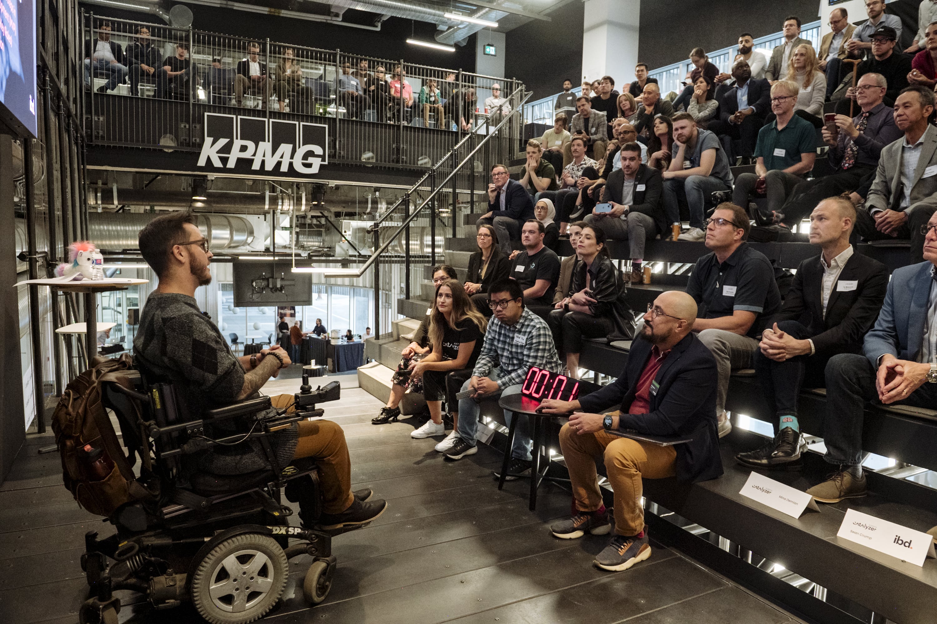 A presenter addresses an audience seated on the tiered KPMG Pitch Stage