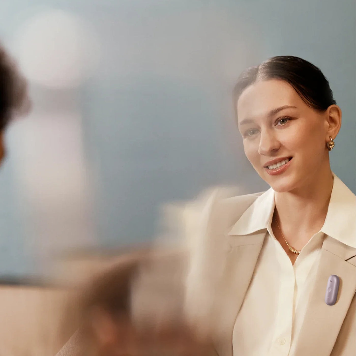 A woman wears a purple Plaud NotePin S on her blazer during a conversation.
